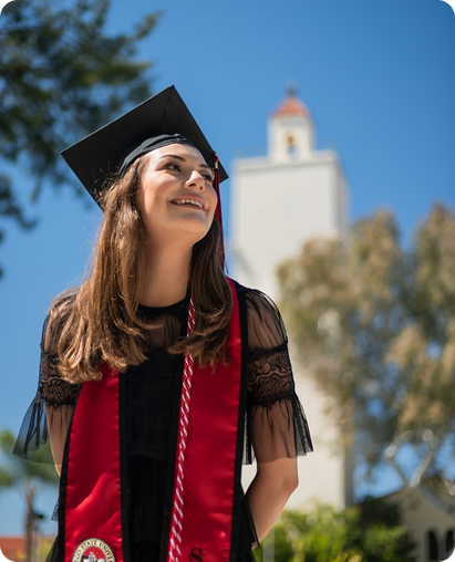 A young woman in a graduation cap and gown looking up.